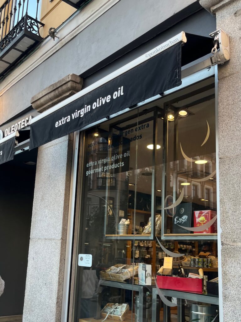 マドリードにあるエクストラバージンオリーブオイル専門店『La Chinata（ラ・チナータ）』の店舗外観。黒いオーニングに“extra virgin olive oil”と記載され、観光客にも人気のスペイン産オリーブオイルを扱う老舗ブランド。