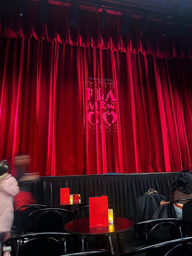 マドリードの人気タブラオ「テアトロ・フラメンコ・マドリード」のステージ。赤いベルベットの幕が閉じた開演前の雰囲気で、前方席から舞台がよく見える。フラメンコショーの臨場感や会場規模がわかる写真。
