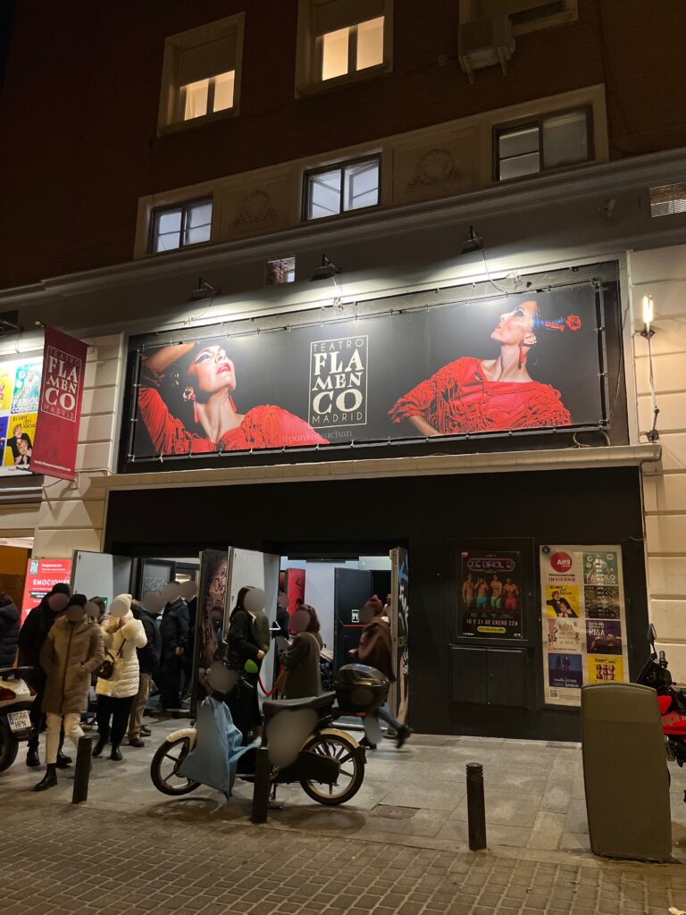 テアトロ・フラメンコ・マドリードの外観。赤い衣装のダンサーが写った看板が掲げられ、夜の公演に入場する観客が列を作っている。アクセスのしやすさや劇場の場所がわかる写真。