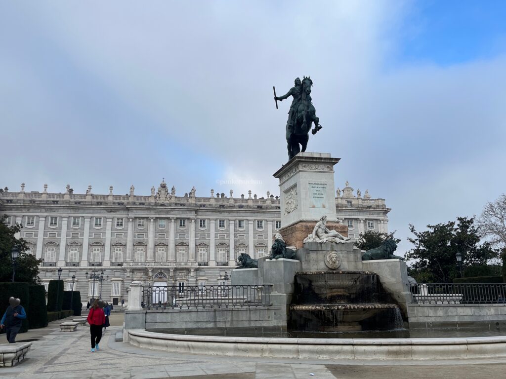 マドリード王宮（パラシオ・レアル・デ・マドリード）の正面外観。広場中央に立つフェリペ4世の騎馬像と、背後に広がる壮麗な白い宮殿建築。